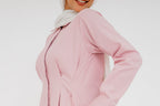 A model wearing a blush pink shirt dress with on a white background. 